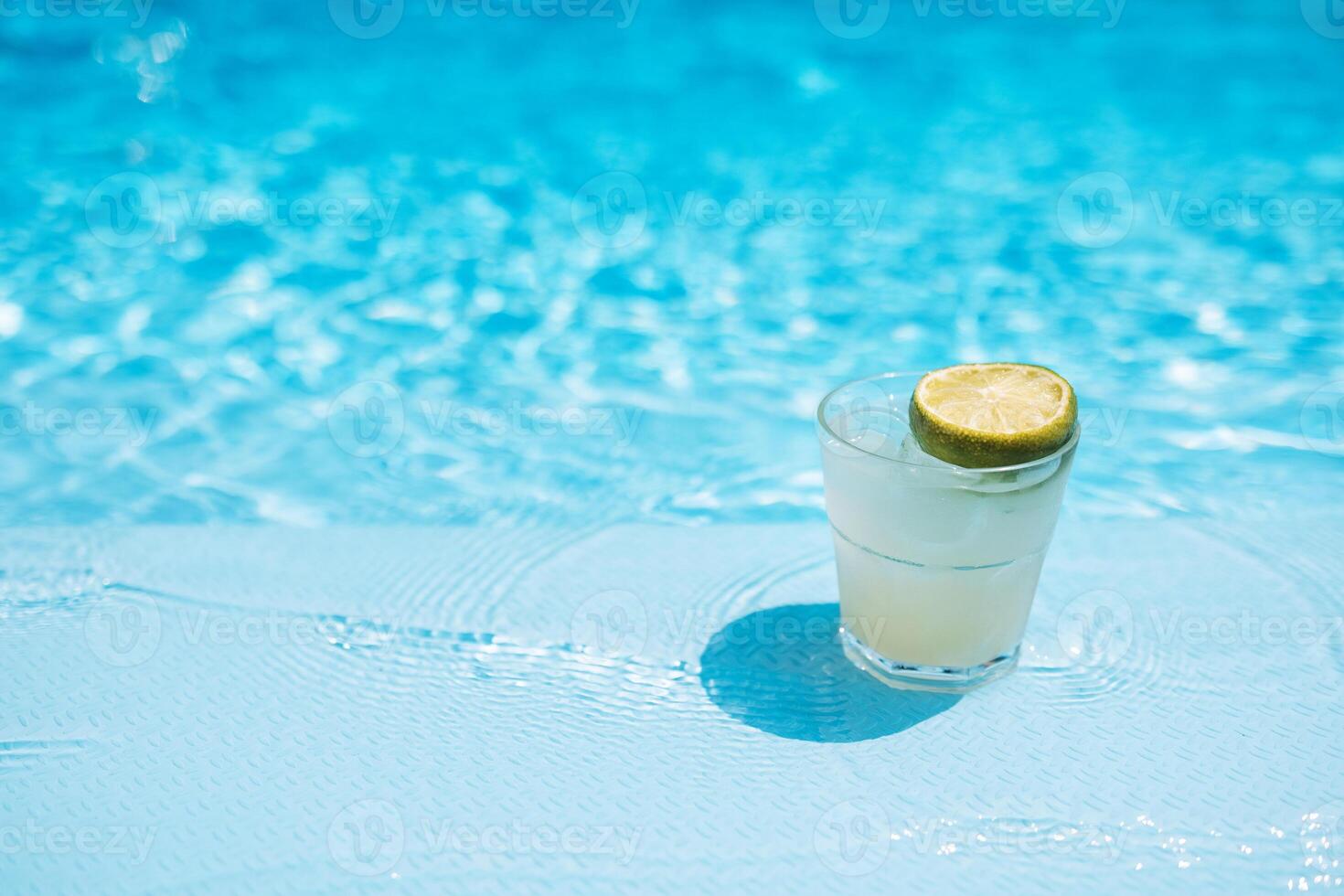 Delicious ice drink with lime, lemon and mint on the side of the pool. Tasty fresh mojito on the background of clear blue water. photo