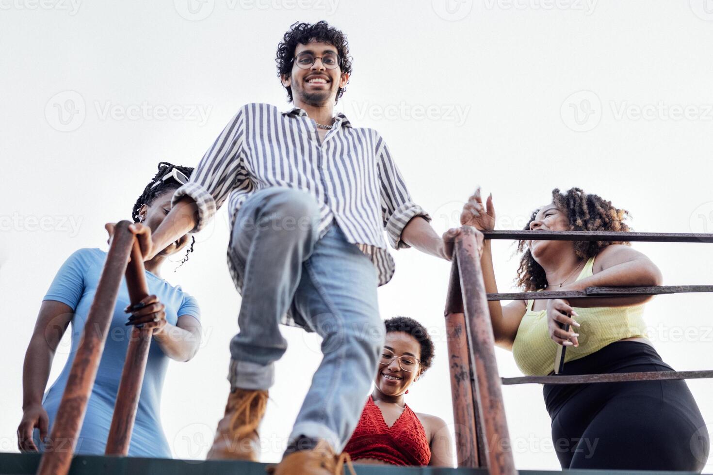 Four cheerful multiethnic friends descend the iron ladder from the roof of the house. Charming African women and a mixed-race man have fun and enjoy weekend. photo