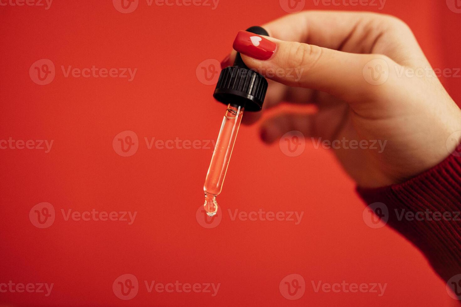 Woman with red manicure holding transparent serum or oil glass pipette. photo