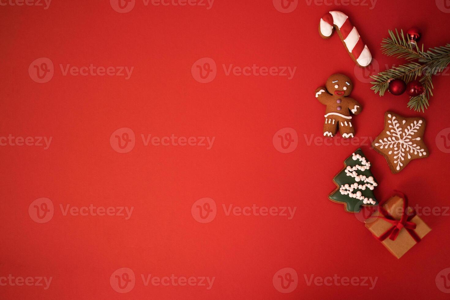Cute red holiday background with cookies, sprig of fir tree with Christmas balls and a gift in craft paper. Cookies in the form of a gingerbread man, a Christmas tree, stars and a candy cone. photo