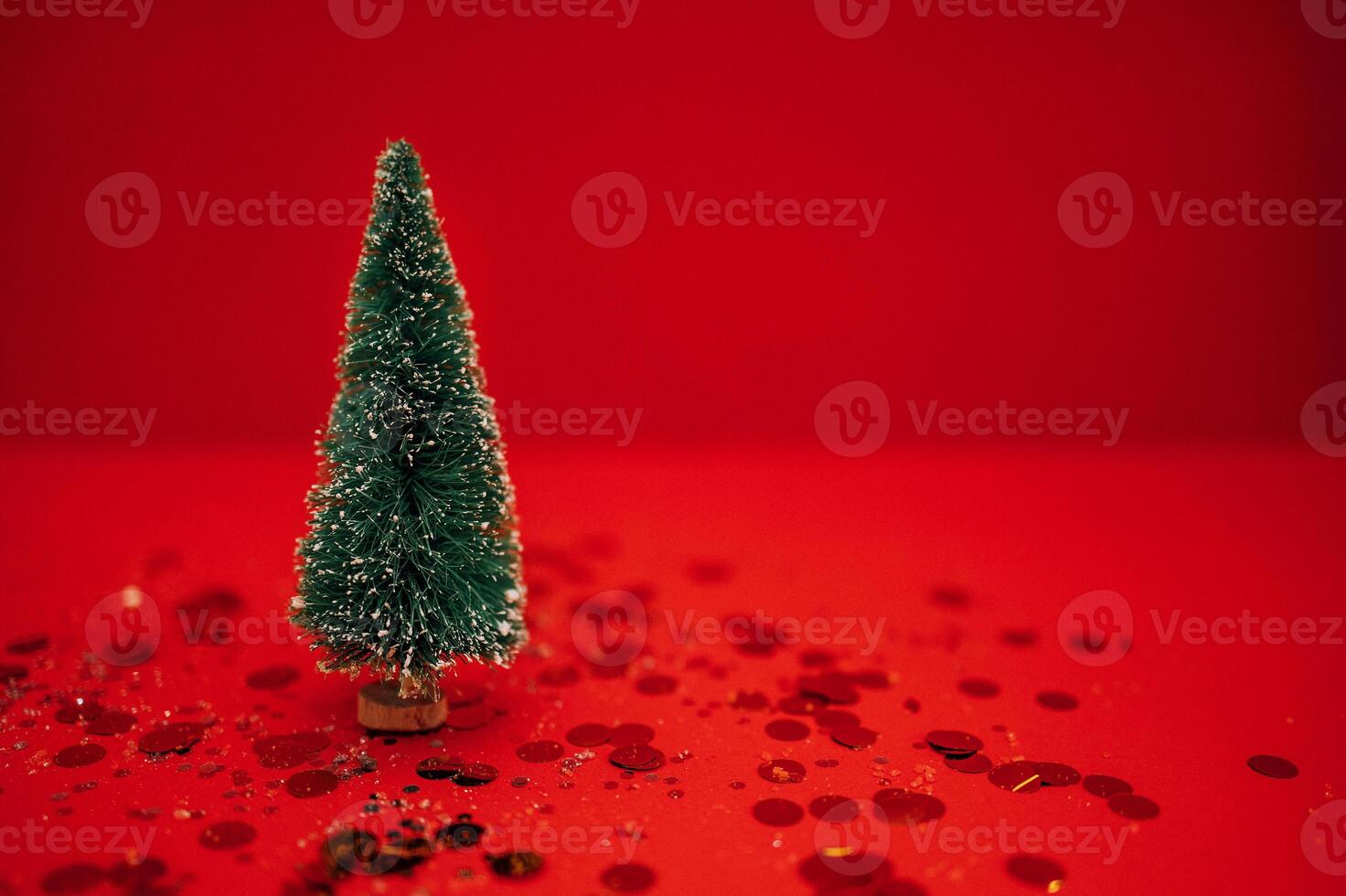 Stylish little Christmas tree on a red background. Bright holiday backdrop with silver glitters and gold round confetti. photo