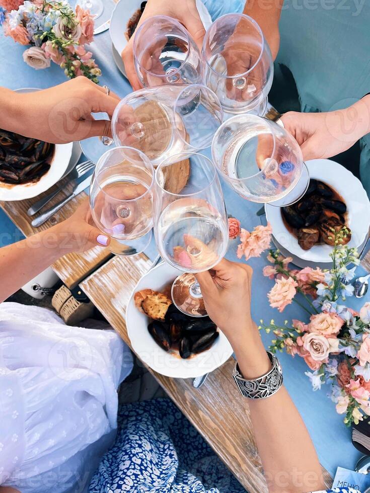 Group of friends cheering with glasses of white wine during picnic with mediterranean food outdoors photo