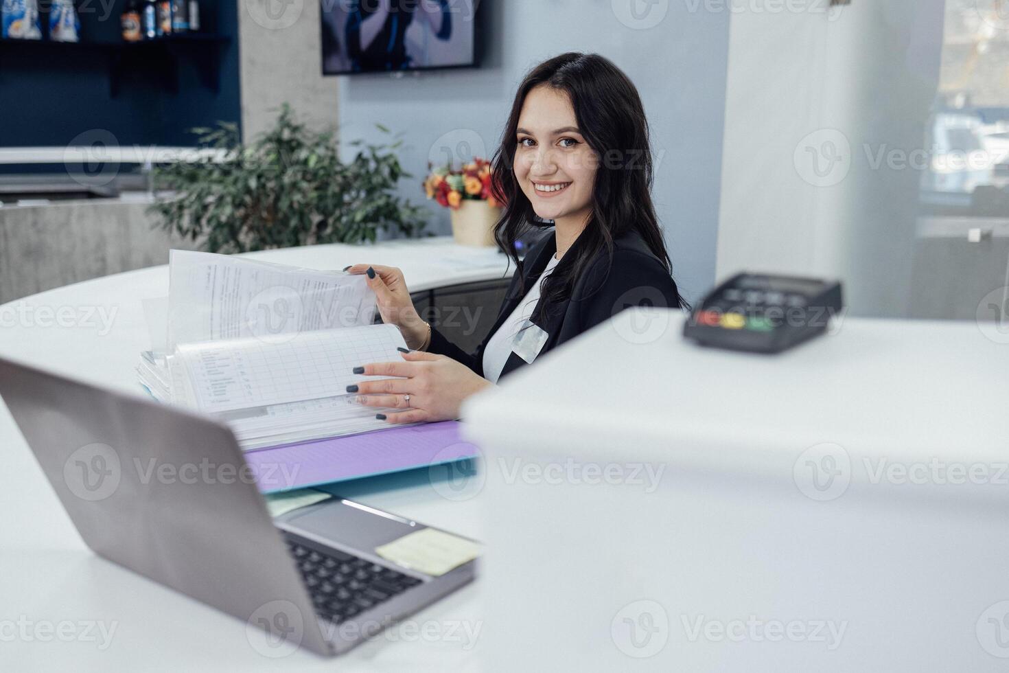 Office female worker in black jacket and white shirt works with catalog of papers and laptop photo