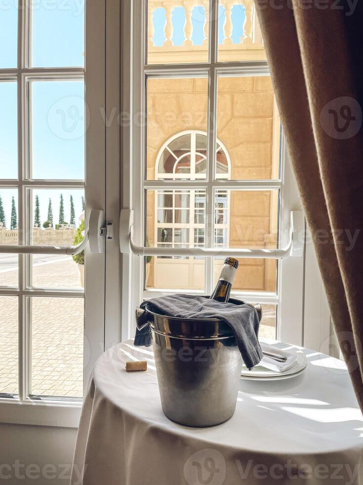Table with white tablecloth, plates, napkins and ice cooler with dark glass bottle of wine photo