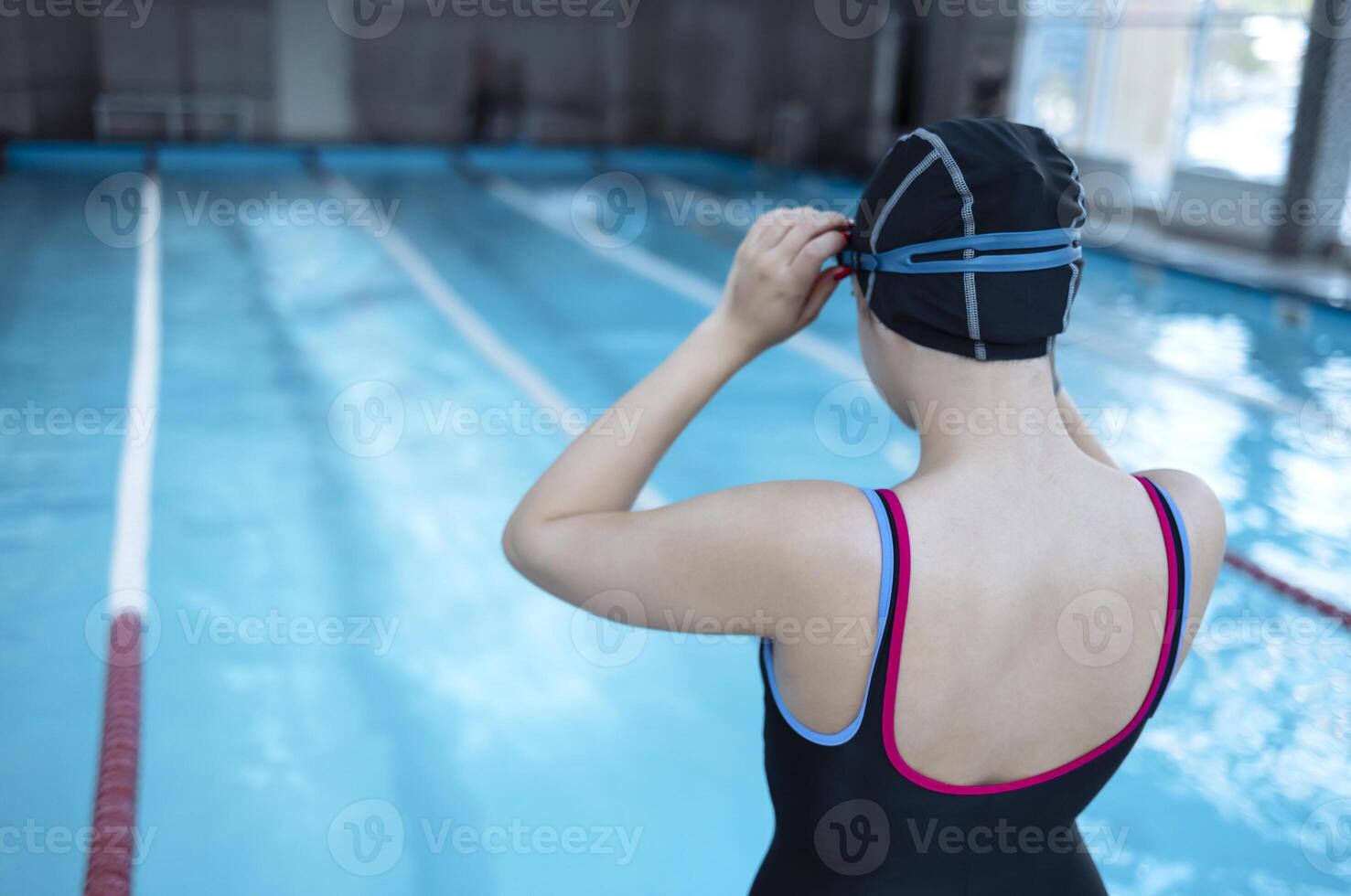 Young swimmer wears a swim cap and puts away goggles photo