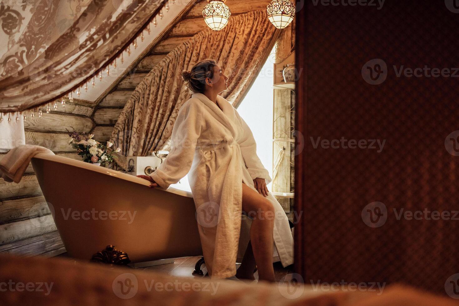 A young woman in a white bathrobe in the hotel bathroom. A charming girl is going to take a bath and enjoy a spa procedure. photo