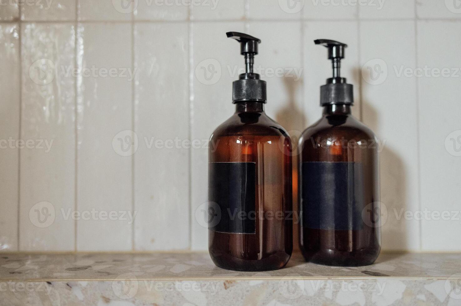 Close-up layouts with brown plastic bottles with dispensers in the bathroom. Mock-ups of shampoo or gel tubes with black empty labels on a background of tiles. photo