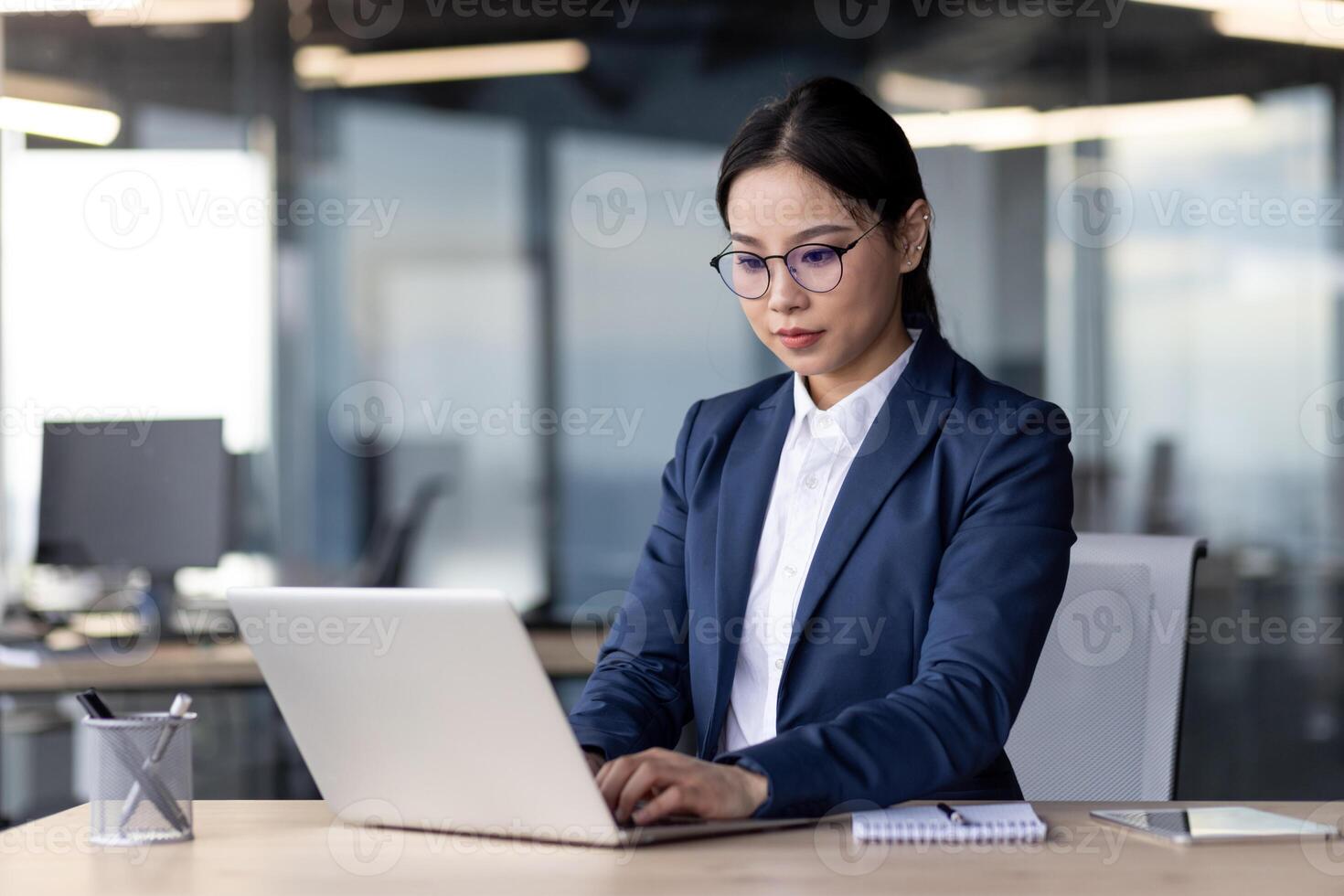 Businesswoman in formal attire working on laptop in modern office. Focused and diligent, she utilizes technology to accomplish tasks efficiently. Office environment reflects modern corporate setting. photo