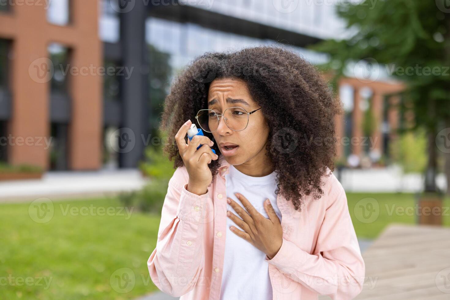 African American woman with using asthma inhaler outdoors. Young woman looking concerned or anxious while using inhaler to manage asthma symptoms. Concept of asthma, health, and respiratory issues photo