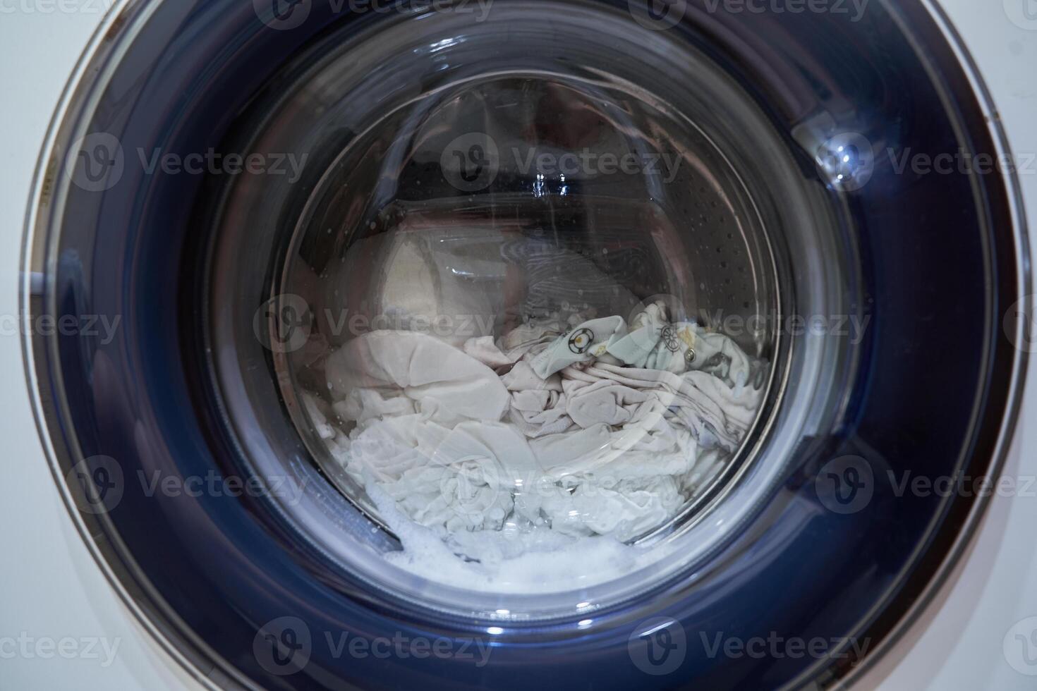 Wet white laundry in the drum of the washing machine. Close-up glass door from the washing machine with space for copying photo