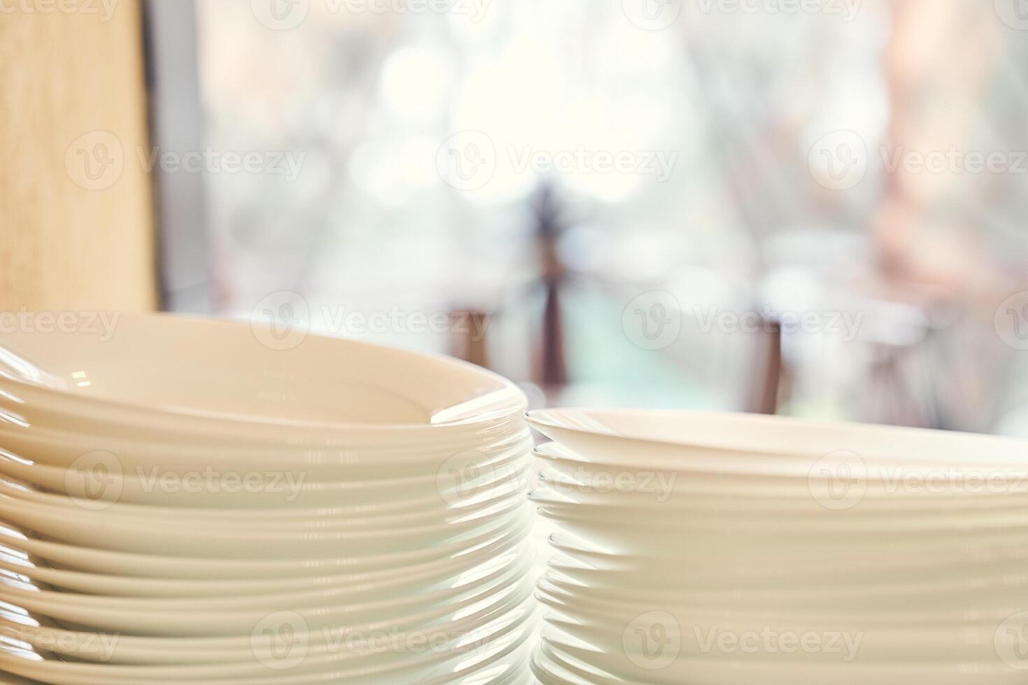 A set of white plates on the table on a light blurred background of the window. Stacks of white dishes on hand at the hotel. photo