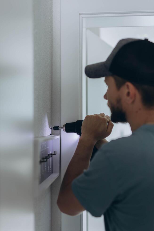 Man with professional tool, screwdriver in hand, at home nails a shelf in the hallway photo