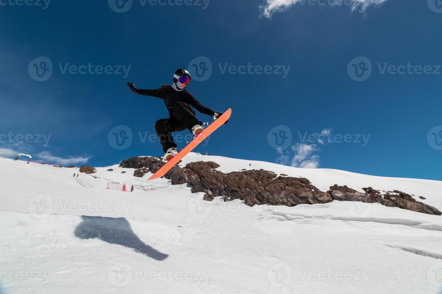 A young woman in a helmet makes a ski jump high in the mountains. Winter sport. Snowboarder woman doing a trick photo