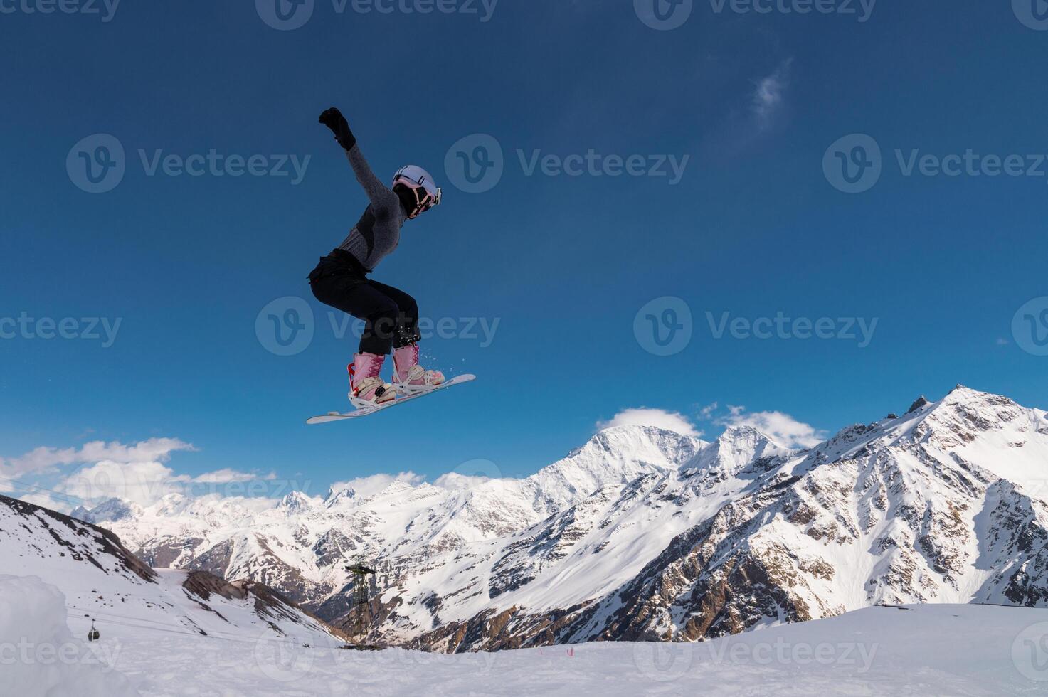 A young woman in a helmet makes a ski jump high in the mountains. Winter sport. Snowboarder woman doing a trick photo