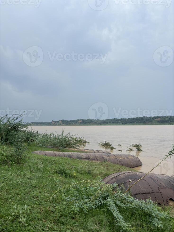 A wide, muddy river stretches across the frame, its waters flowing steadily towards the horizon. photo