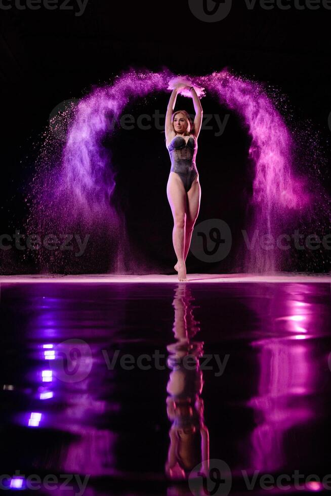 Young slim woman posing with purple particles sprayed in the air photo