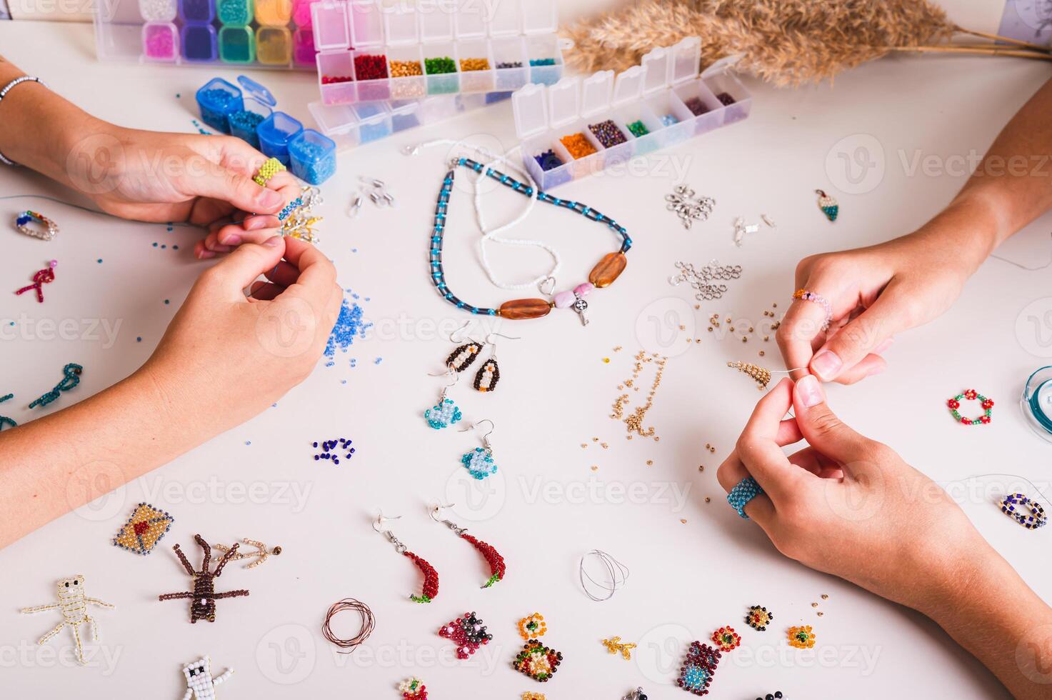 Two girls weaving beadwork on a work table with beading supplies photo