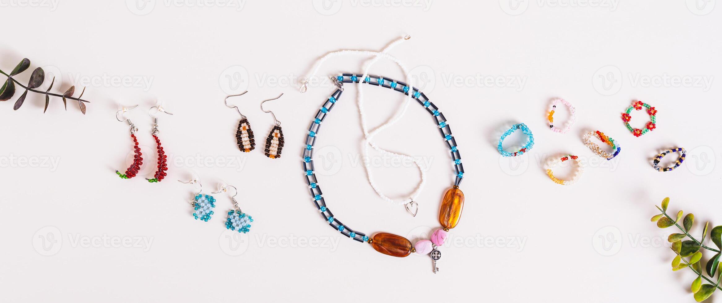Woven from multicolored beads necklaces, earrings and rings on a pink background top view web banner photo