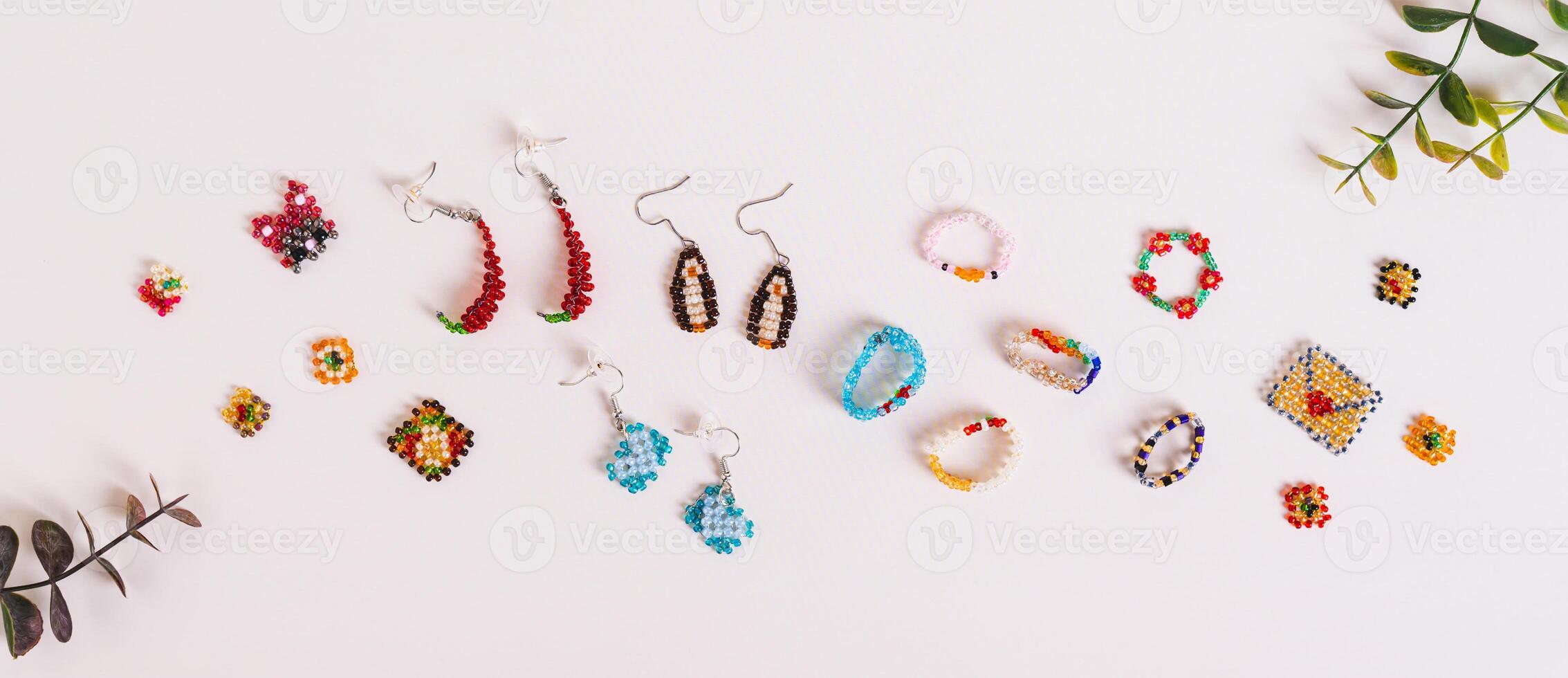 Earrings, rings and toys woven from multi-colored beads on a pink background top view web banner photo