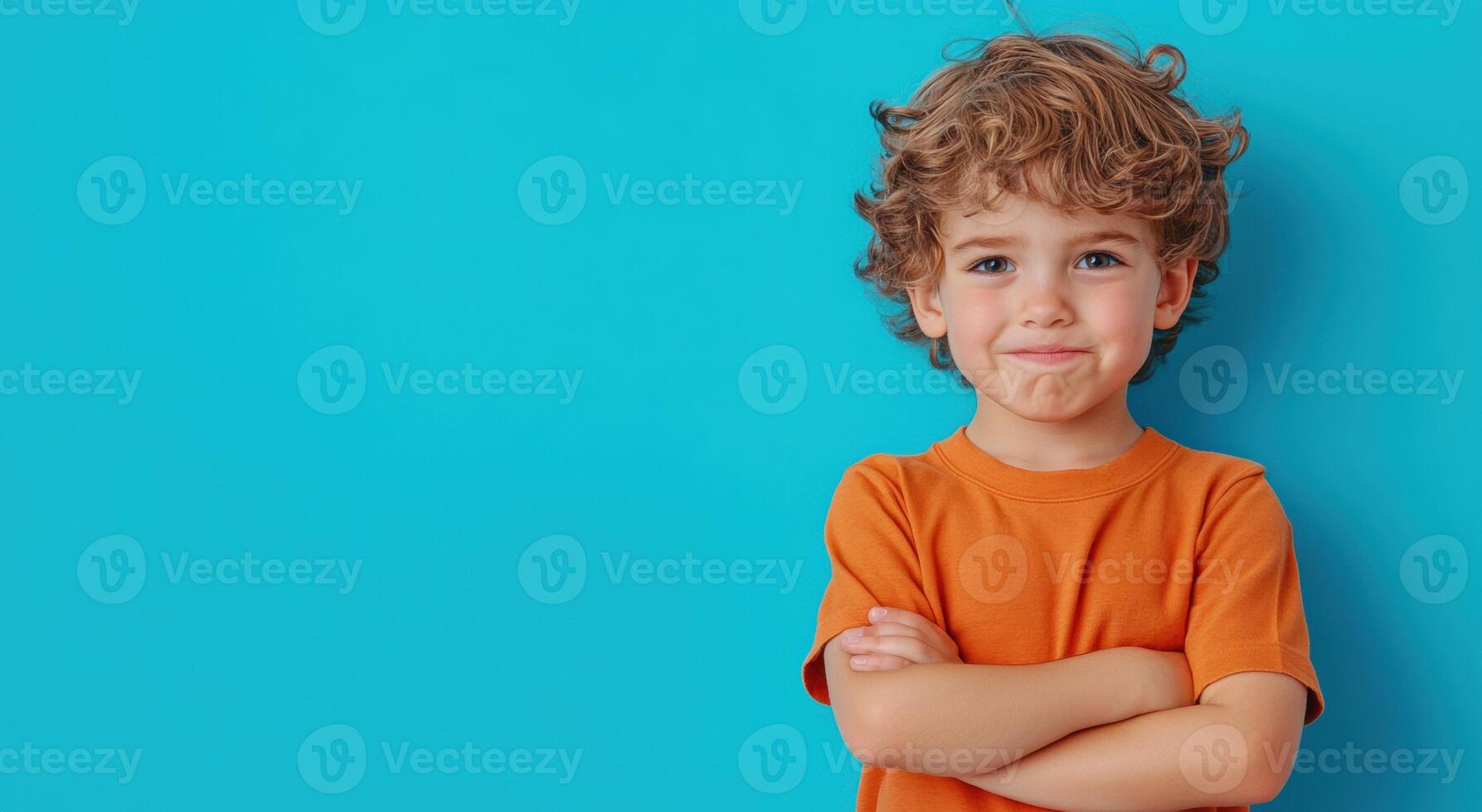 A cheerful boy with curly hair poses confidently in front of a bright blue background, showcasing a playful spirit. photo