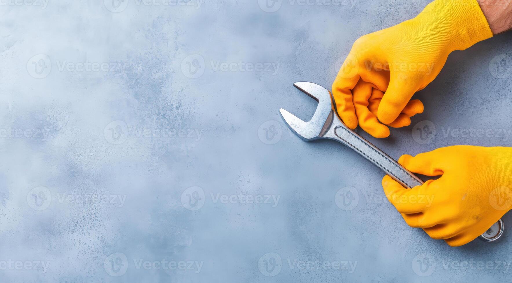 Close-up of hands in yellow gloves holding a wrench on a textured blue background, perfect for maintenance and repair themes. photo