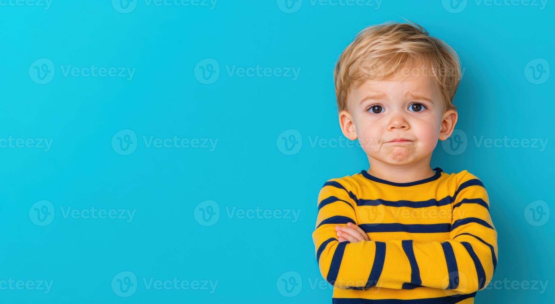 A young boy with a thoughtful expression stands against a vibrant blue background, showcasing innocence and curiosity. photo