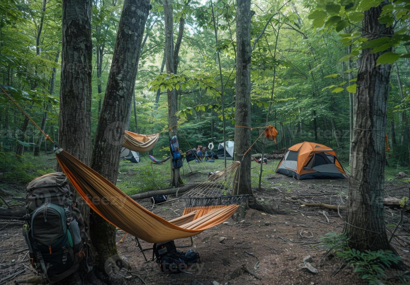 A well organized campsite featuring a hammock strung between trees, a backpack, and a nearby tent photo