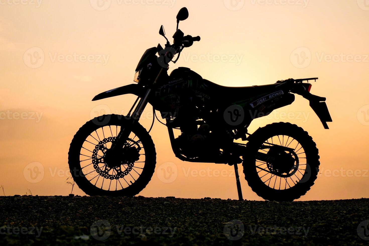 Silhouette of a Dirt Bike Against a Golden Sunset Sky on a Gravel Path photo