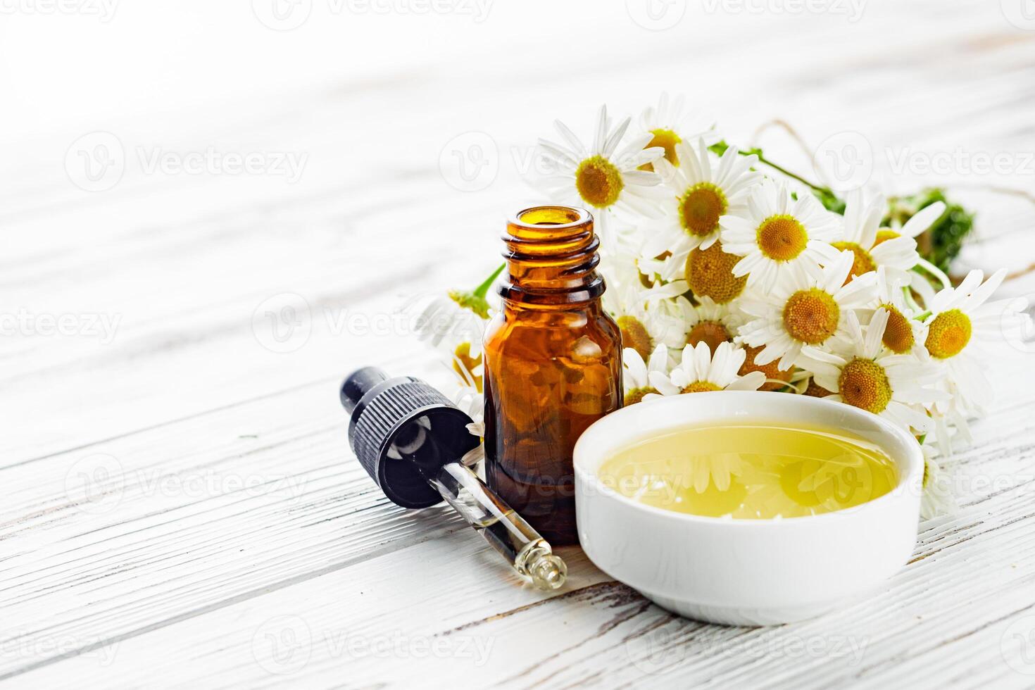 aromatic chamomile essential oil on a white wooden rustic background photo