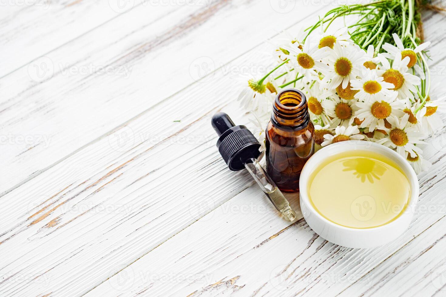 aromatic chamomile essential oil on a white wooden rustic background photo