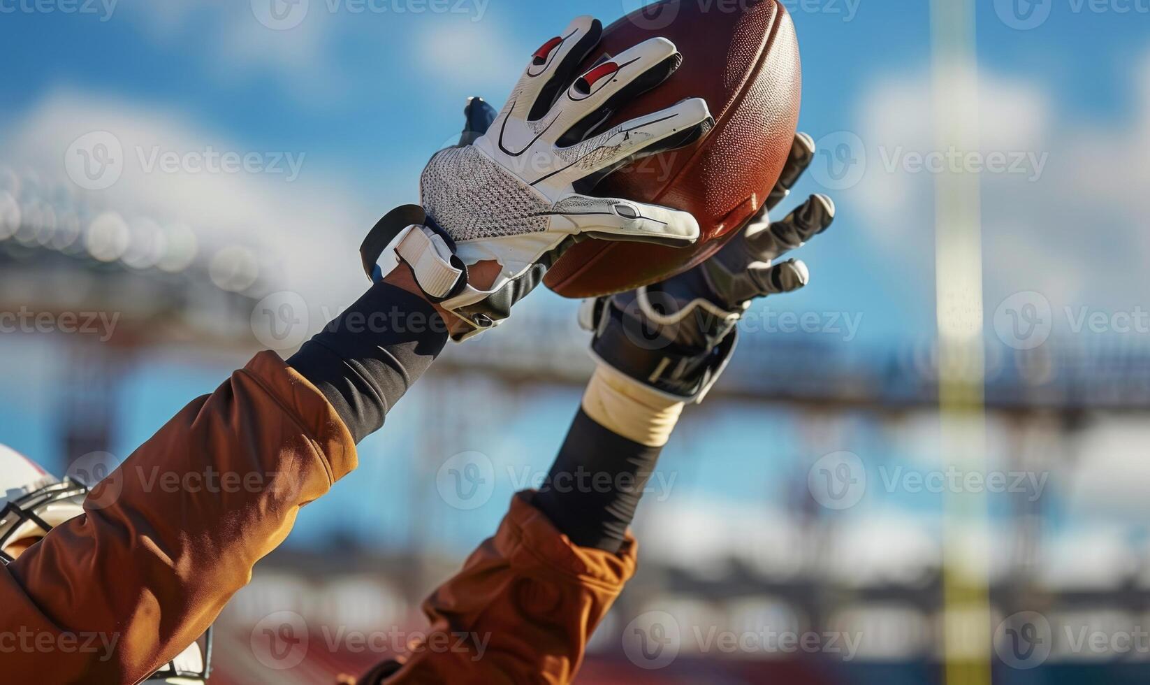 A football player's hands catching the ball mid-air, with the field and goalposts in the background photo