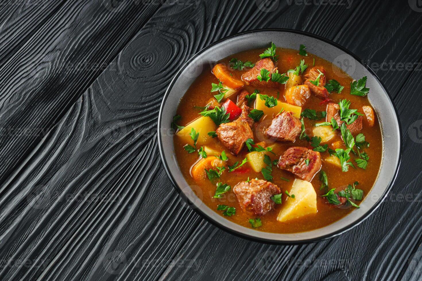 fragrant thick goulash soup on a black wooden rustic background photo