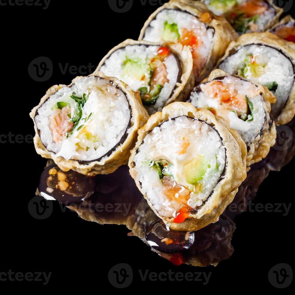 hot sushi roll tempura with salmon cream cheese cucumber avocado unagi on a black mirror background photo