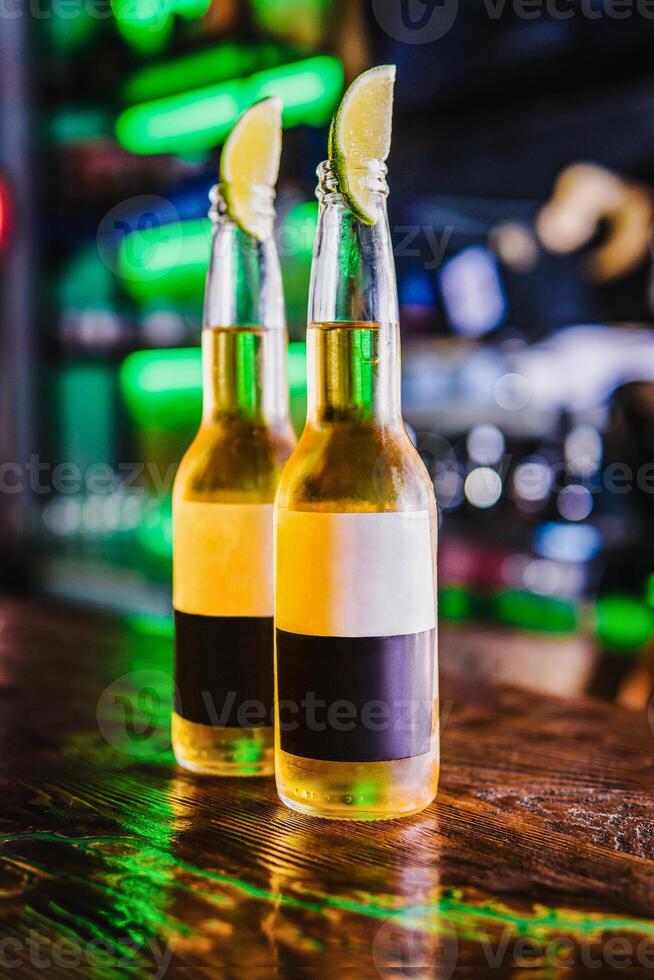 Cold light beer in bottles on the bar. Lime wedges cover the necks of the bottles. photo