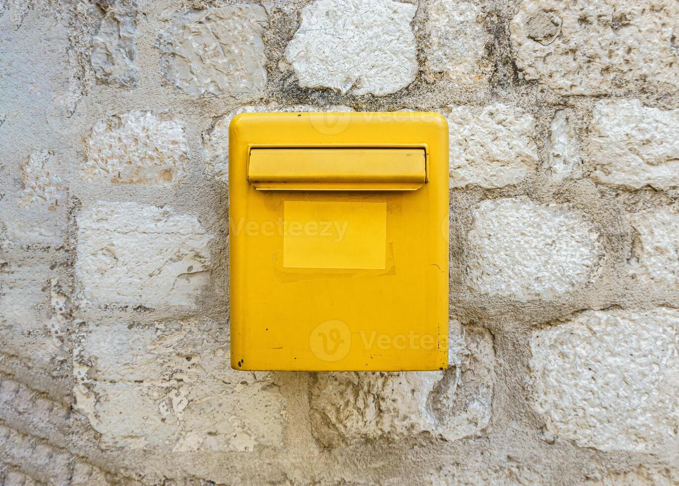 A yellow mailbox on a light stone wall. Box for letters and postcards. photo