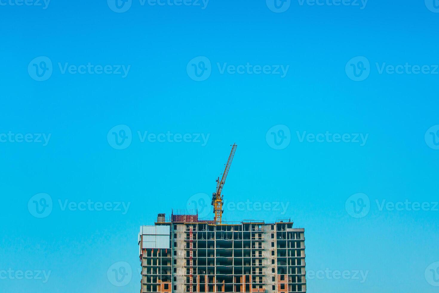 Under construction high-rise building with yellow construction crane in the sunlight. Construction work site and high rise crane building. photo