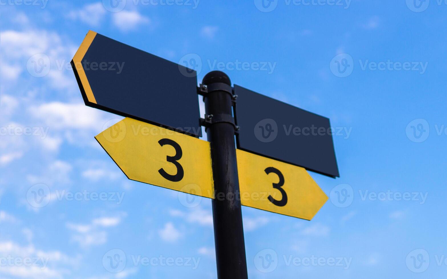 Yellow direction sign on the pole against the blue sky. Yellow arrow signal against sky. photo