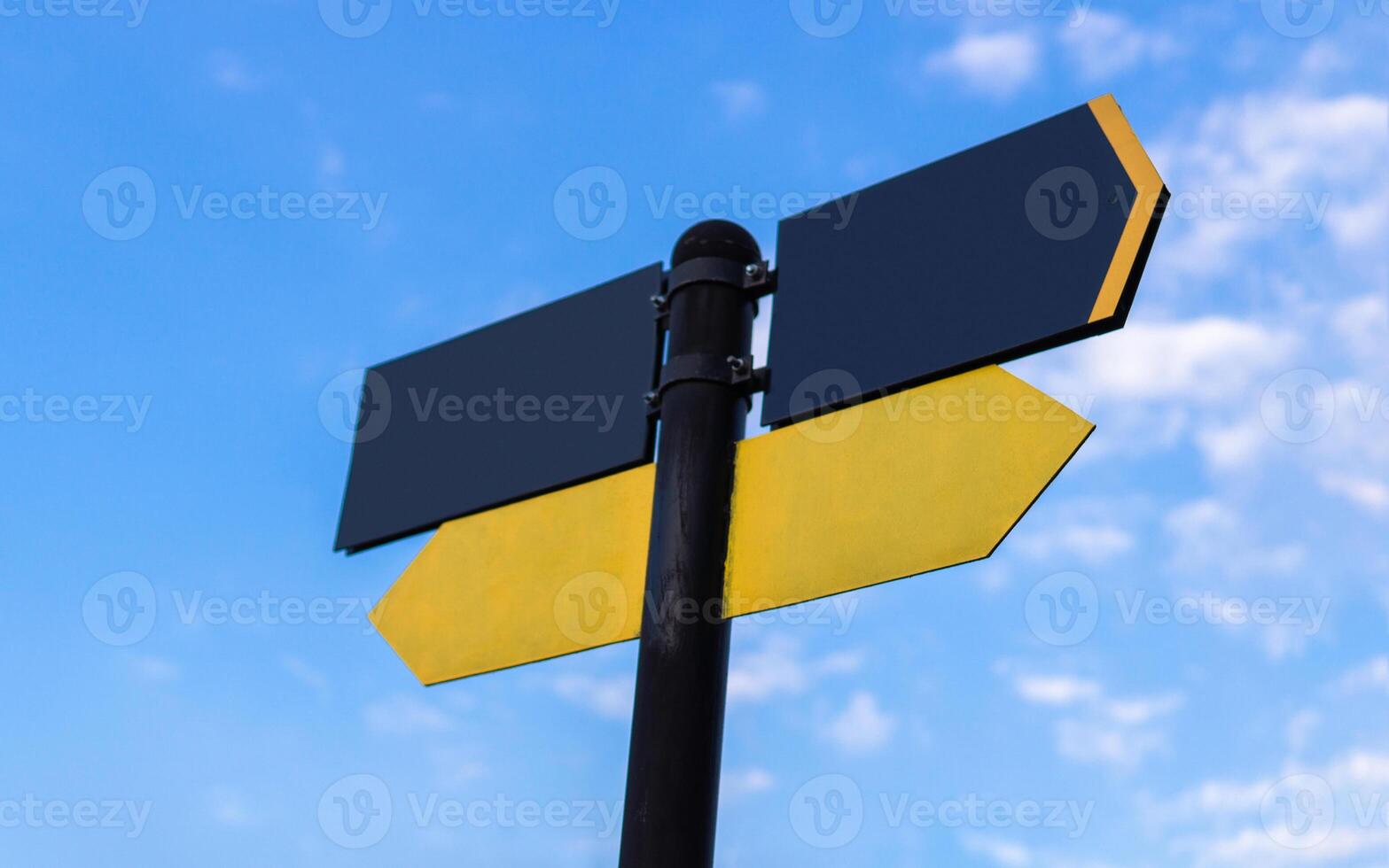 Yellow direction sign on the pole against the blue sky. Yellow arrow signal against sky. photo
