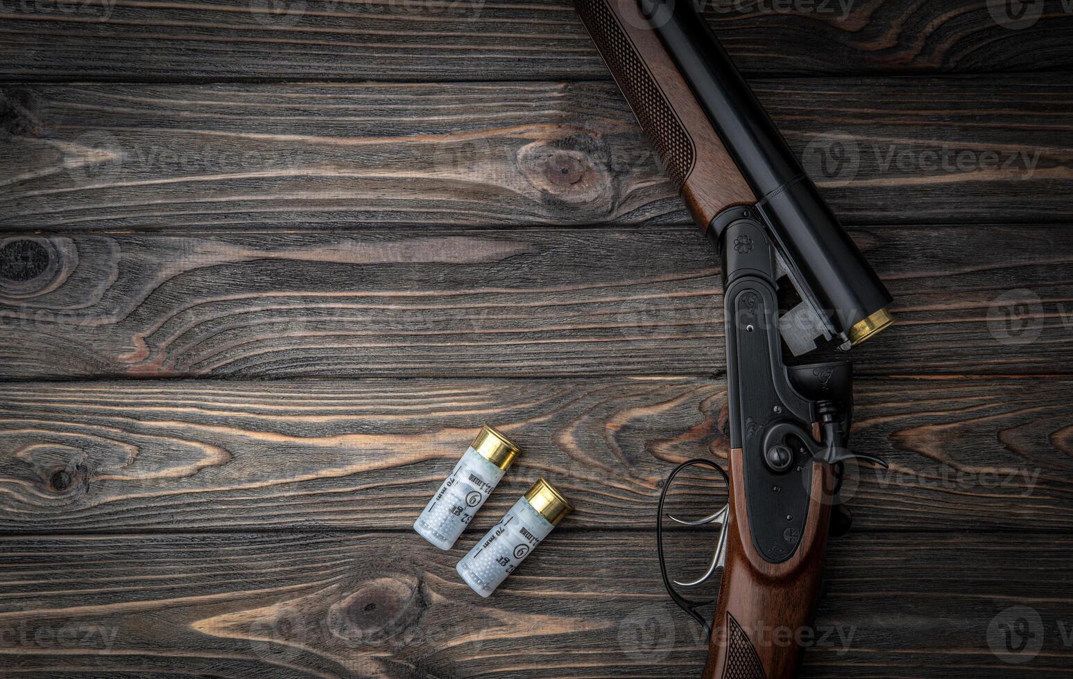 Opened double-barreled hunting rifle on a wooden table. Shotgun ammo. Dark brown wooden back. photo