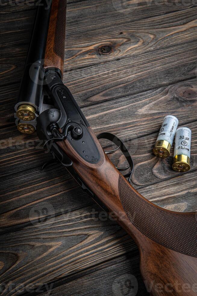 Opened double-barreled hunting rifle on a wooden table. Shotgun ammo. Dark brown wooden back. photo