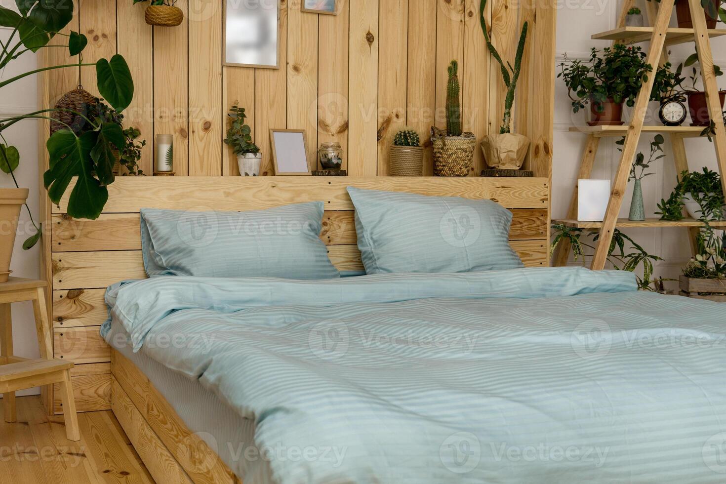 Real photo of a botanical bedroom interior with wooden shelves, double bed and plants. Bedroom wooden interior with plants next to a bed made with pillows.