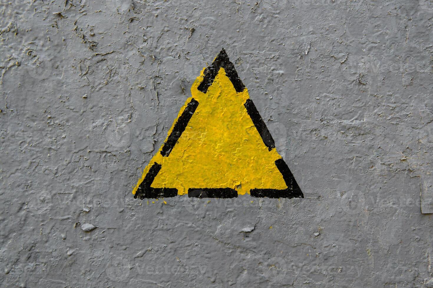 Yellow triangle on a old gray coarse metaic painted surface photo