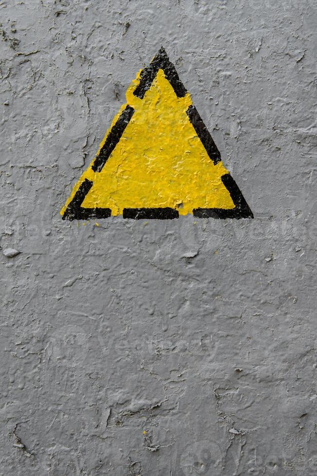 Yellow triangle on a old gray coarse metaic painted surface photo