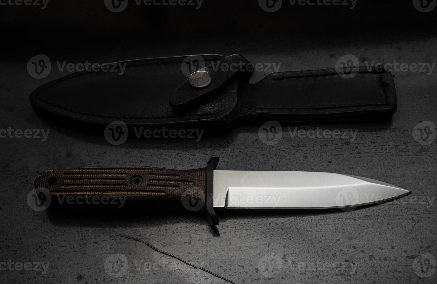 A modern hunting knife and a leather case for him on a dark background. Melee weapons for hunting and self-defense. The instrument of crime. photo