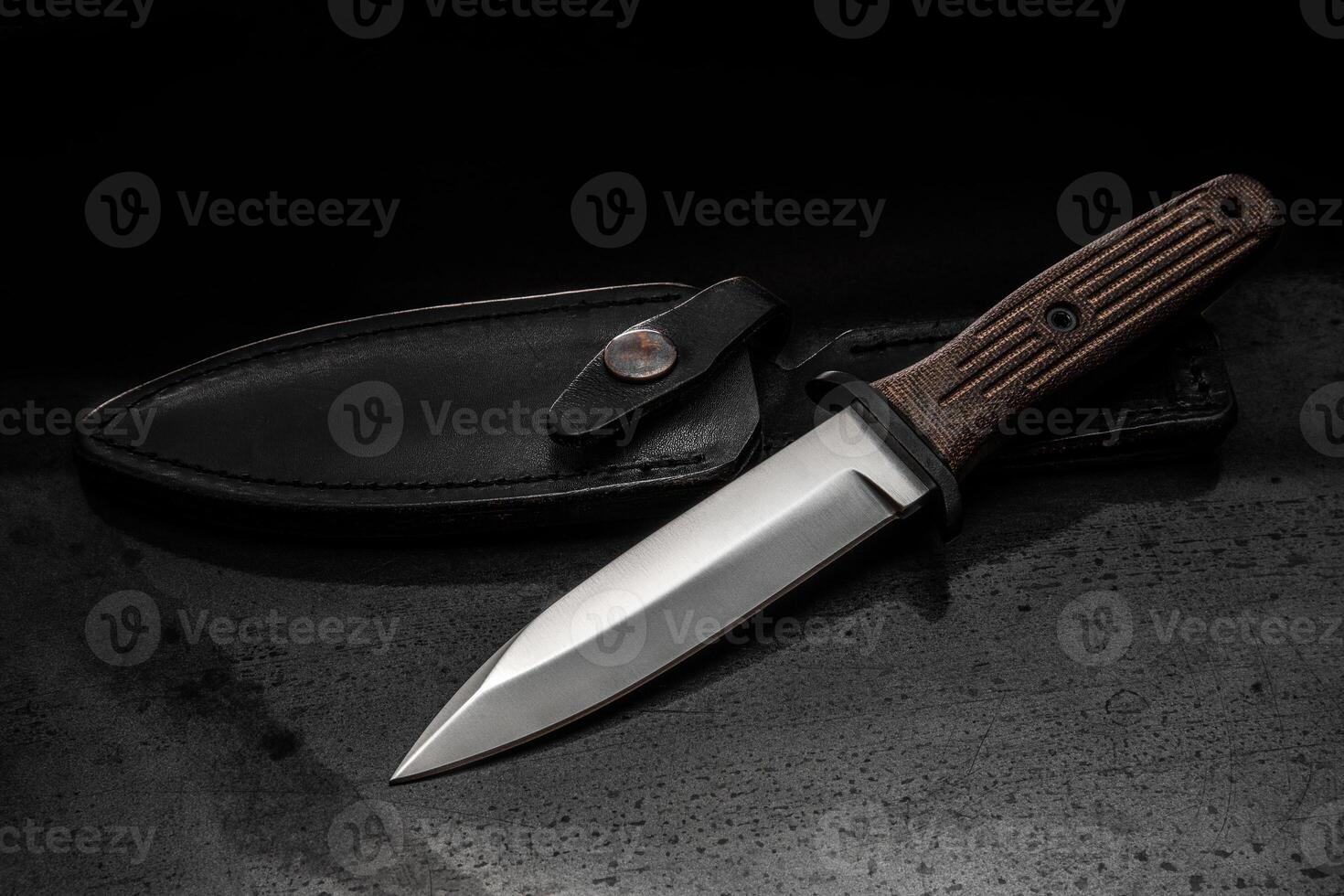 A modern hunting knife and a leather case for him on a dark background. Melee weapons for hunting and self-defense. The instrument of crime. photo