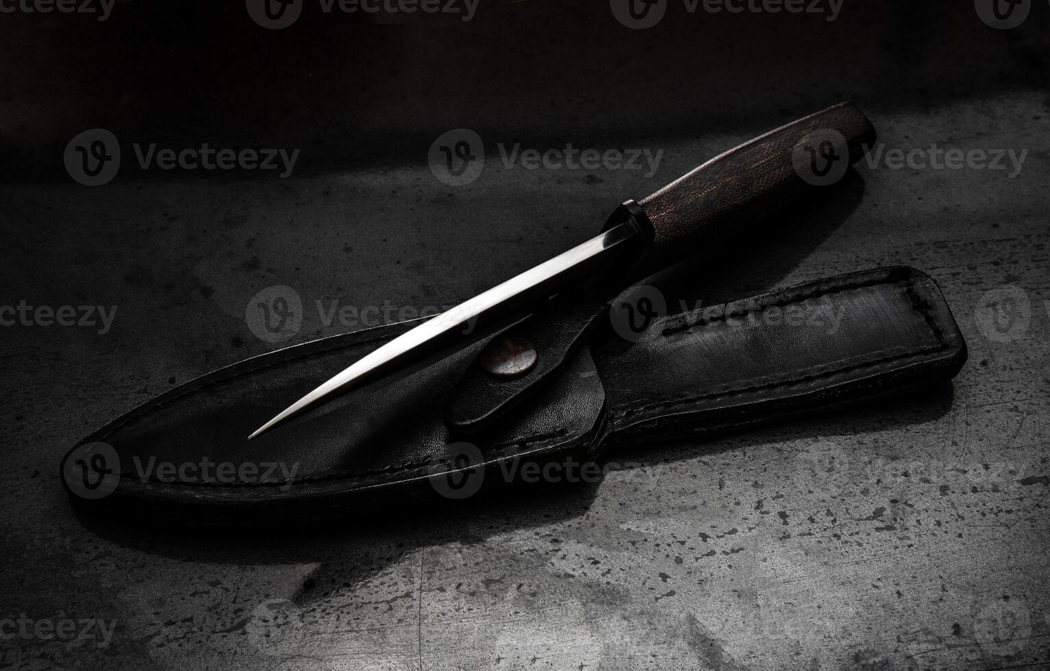 A modern hunting knife and a leather case for him on a dark background. Melee weapons for hunting and self-defense. The instrument of crime. photo