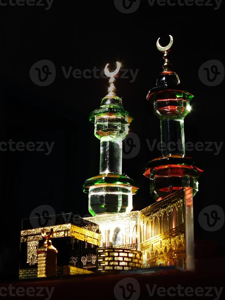Small model of the Kaaba, the holy mosque of the Grand Mosque, Mecca, isolated on a dark background. There is sunlight coming performing an amazing shadow and shining reflection photo
