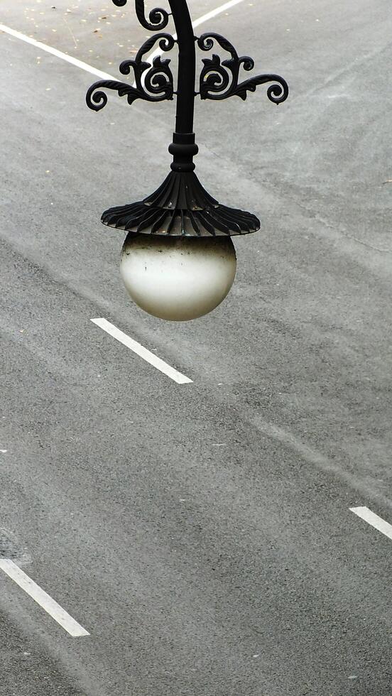 A street light with a white shade is hanging from a pole on the asphalt street road. The light is surrounded by a white line. Copy space for text photo