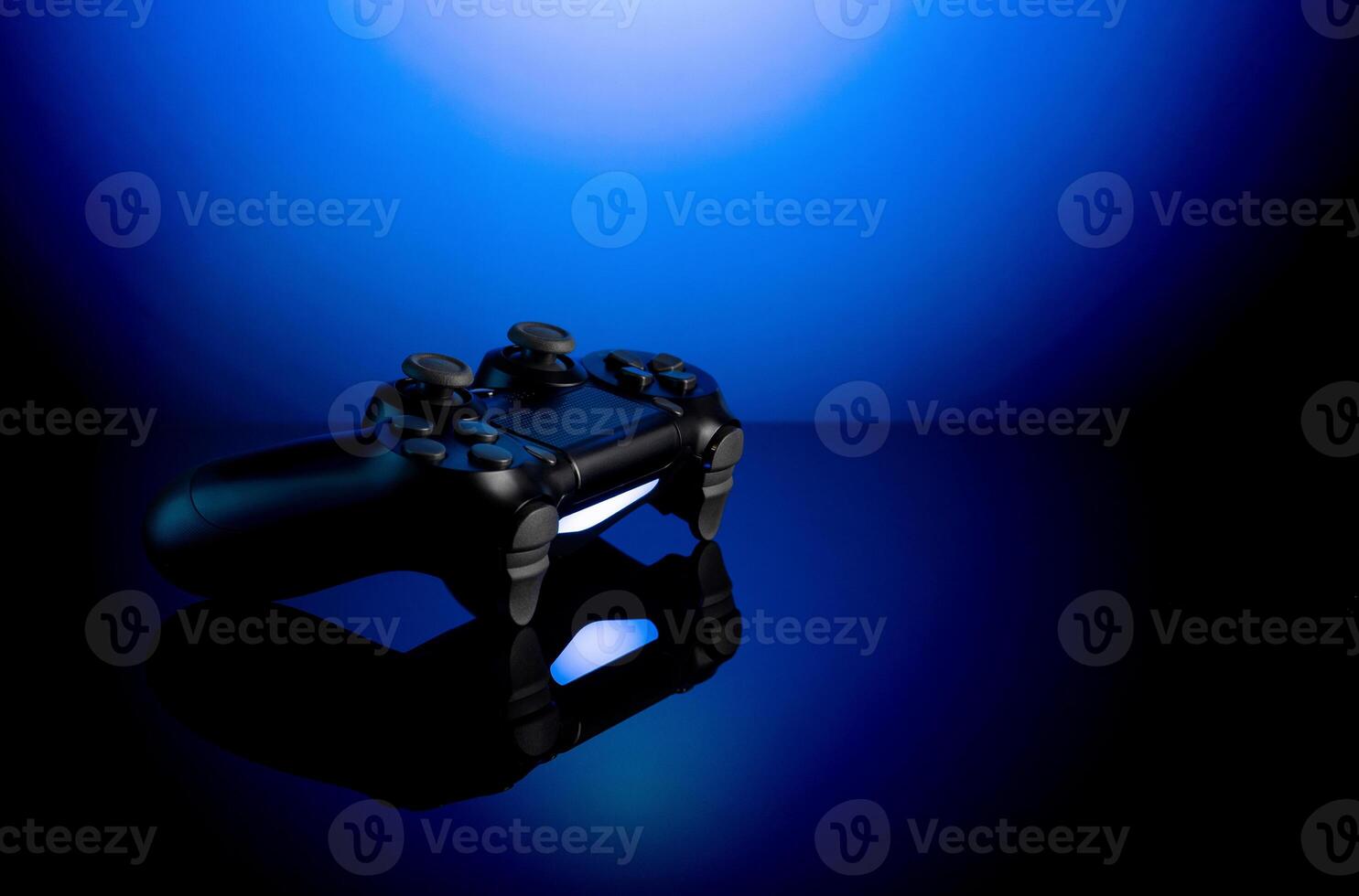 Black gamepad with backlight on blue back. Joystick on glossy surface. photo