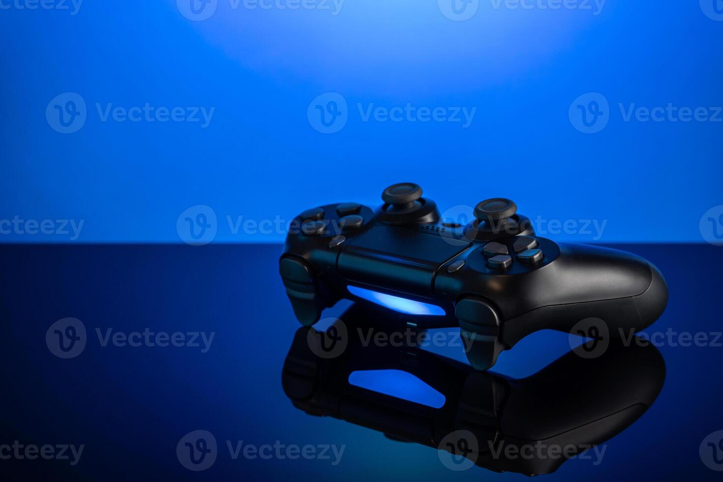 Black gamepad with backlight on blue back. Joystick on glossy surface. photo